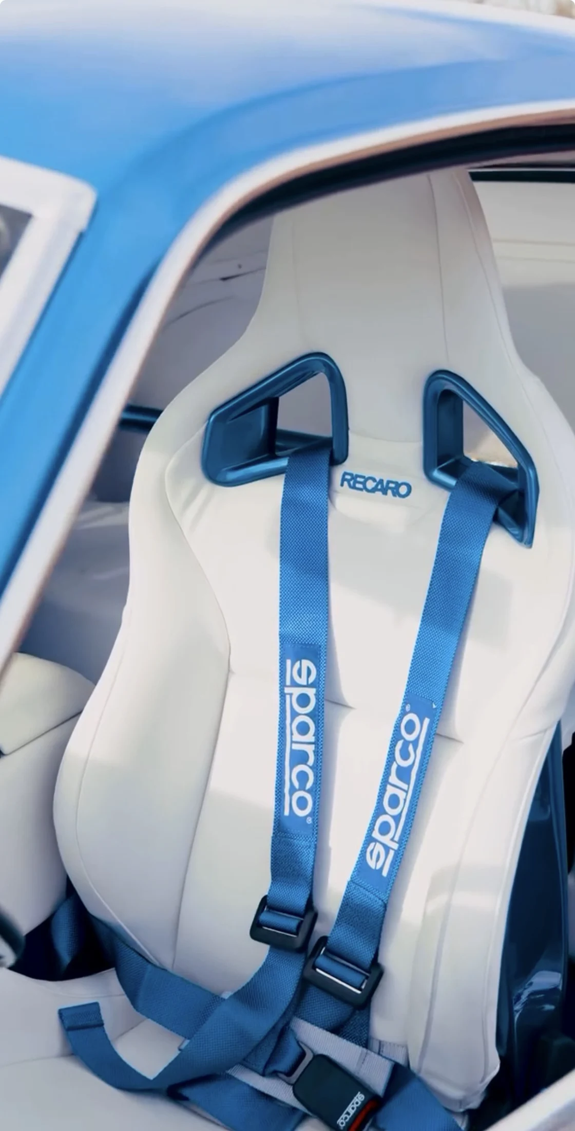 White Recaro seat with blue trim and Sparco harness